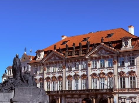 The Jan Hus memorial in front of the Kinský Palace under a blue sky